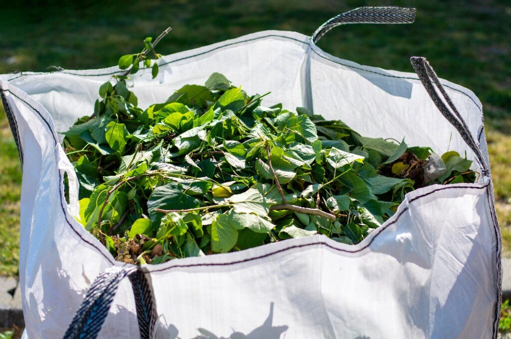 Großer weißer Mietsack mit grünem Bio-Gartenabfall.